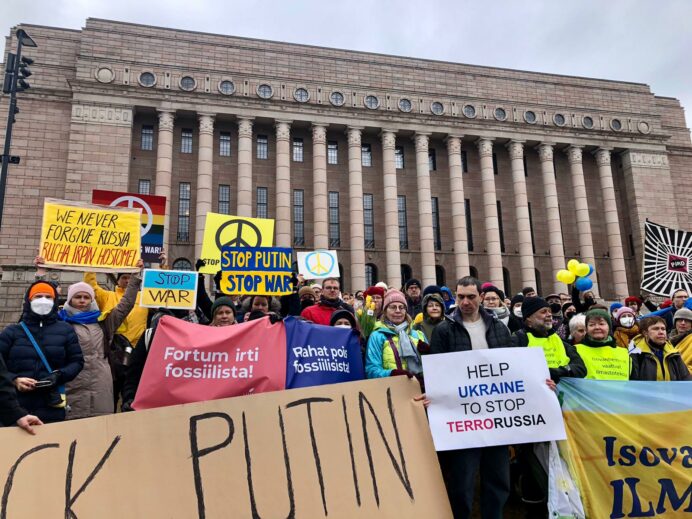 Mielenosoittajia Eduskuntatalon edessä. Bannereissa ja kylteissä on Venäjän hyökkäyssodan vastaisia iskulauseita sekä Hiilivapaa Suomen Fortum-bannereita.